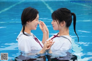 Two young women in a swimming pool with their hands together.