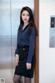 A woman in a blue shirt and black skirt standing in an elevator.