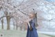 A woman in a blue dress standing next to a tree with white flowers.