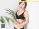 A woman in a black bra and panties holding a plant.